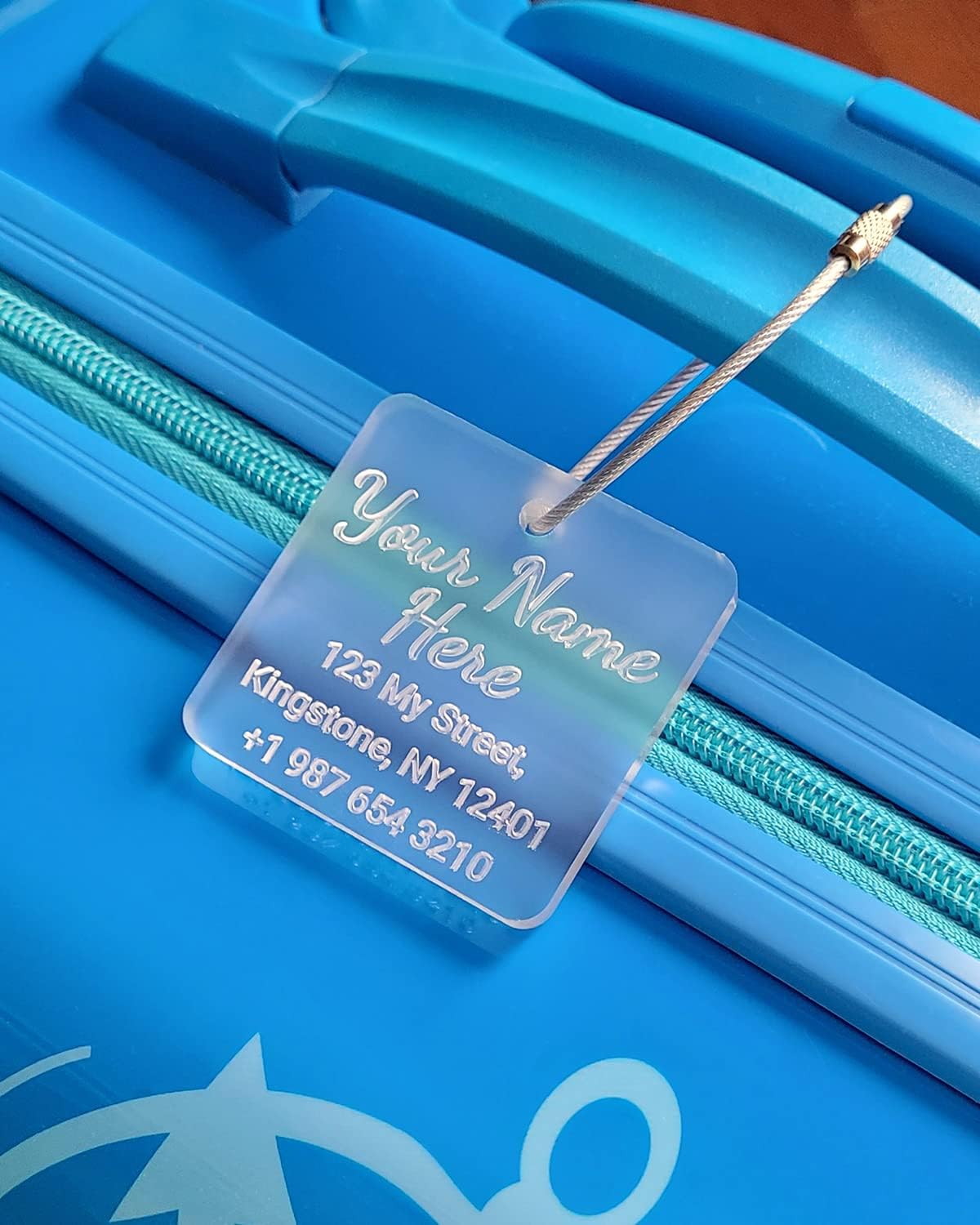 Clear acrylic luggage tag on blue suitcase with cursive engraving